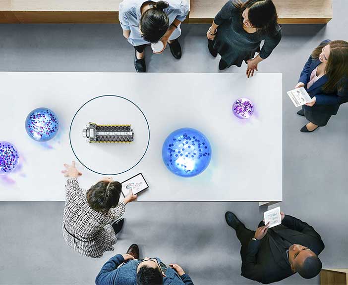 A bird's eye view of people around table with model of an engine