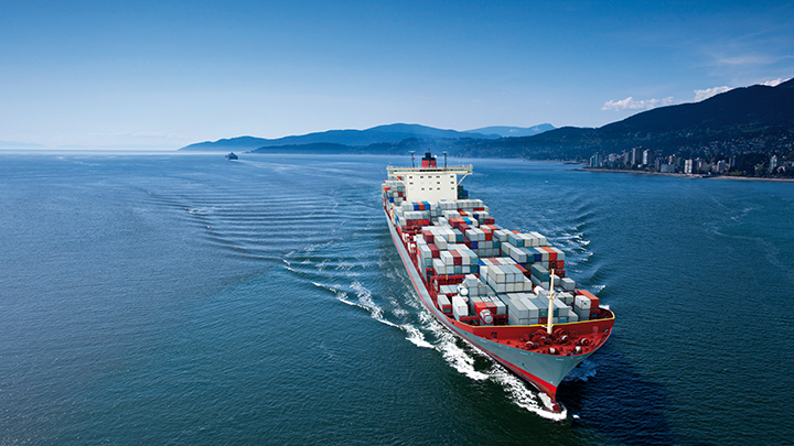 Cargo ship loaded with containers sailing away, with mountains and coastline in the background