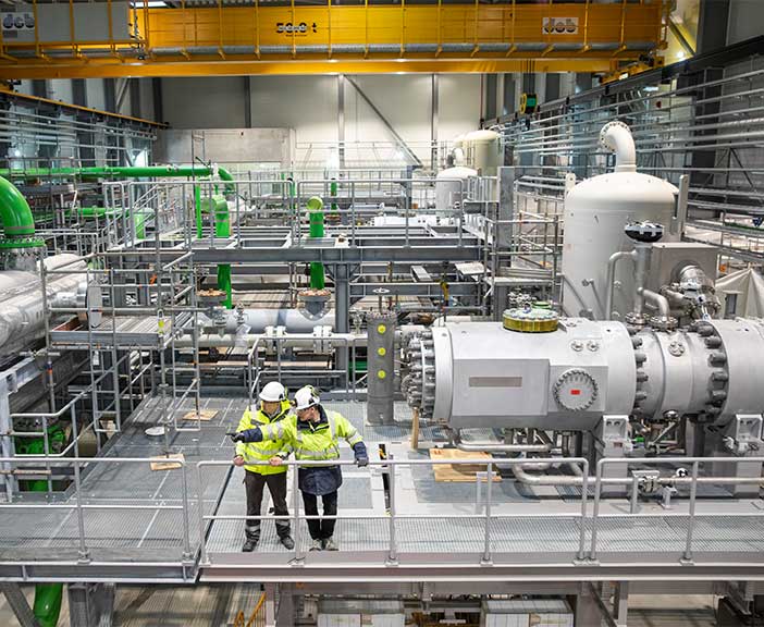 two men standing in front of heat pump in power station