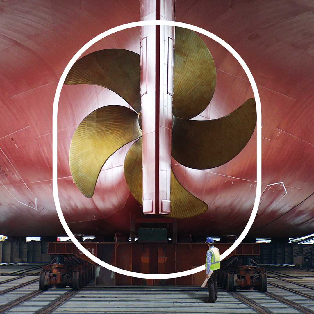 Man standing in front of a large ship's propeller
