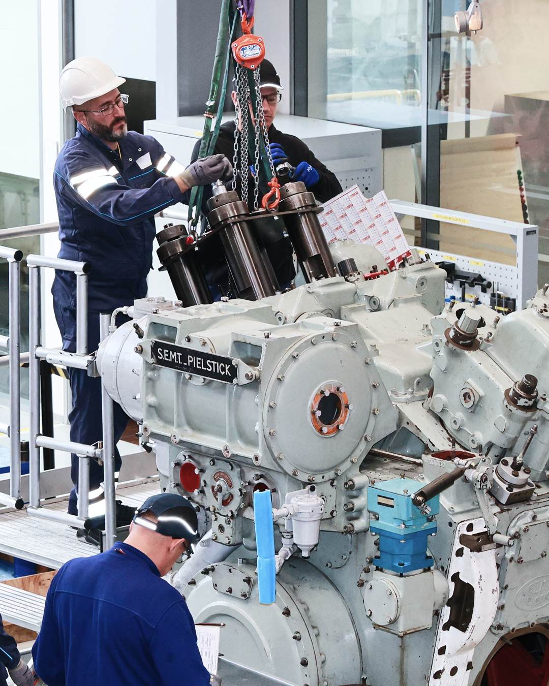 Technicians performing maintenance on a SEMT Pielstick engine at a service facility.