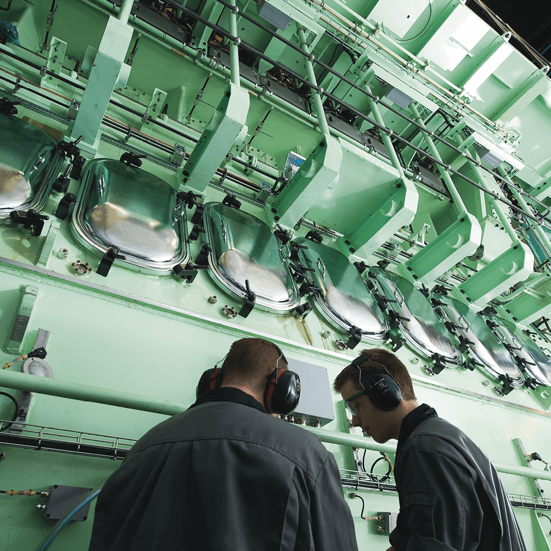 two workers in front of a big marine engine