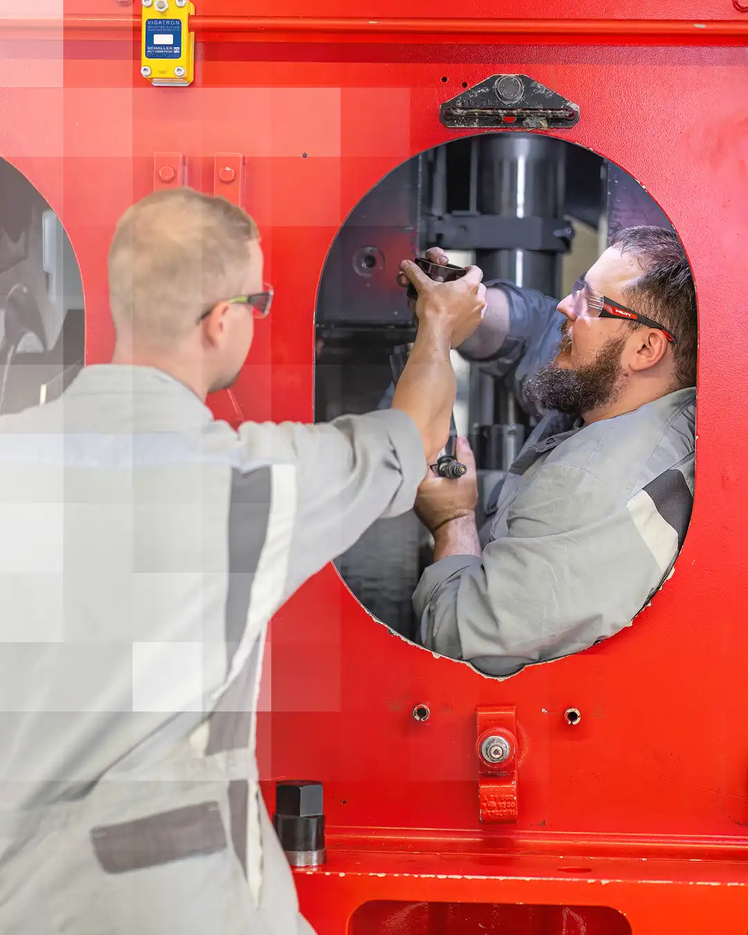 Technicians adjusting equipment through an opening in a red machine.