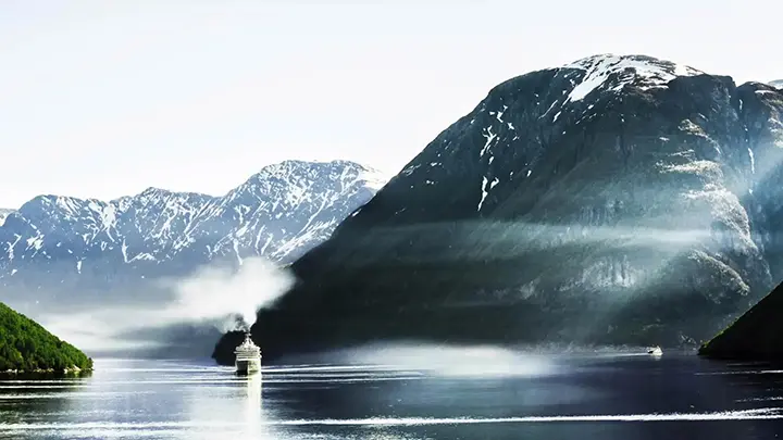 A ship sails through a fjord landscape